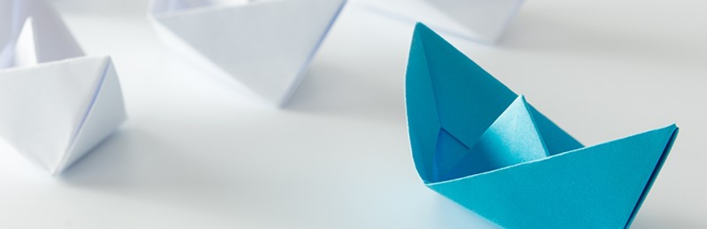 A blue paper boat leads ahead of rows of white paper boats