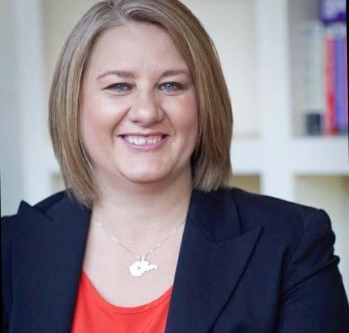 Woman with blonde hair, a red shirt and Black blazer smiling 