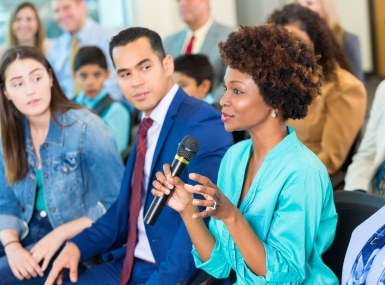 A woman speaks into a microphone while others listen in