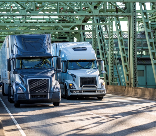 Industrial carriers blue and white big rig semi-truck tractors transporting cargo on dry van semi-trailers running on the truss metal arch I-5 Interstate Bridge between Washington and Oregon across  the Columbia River.