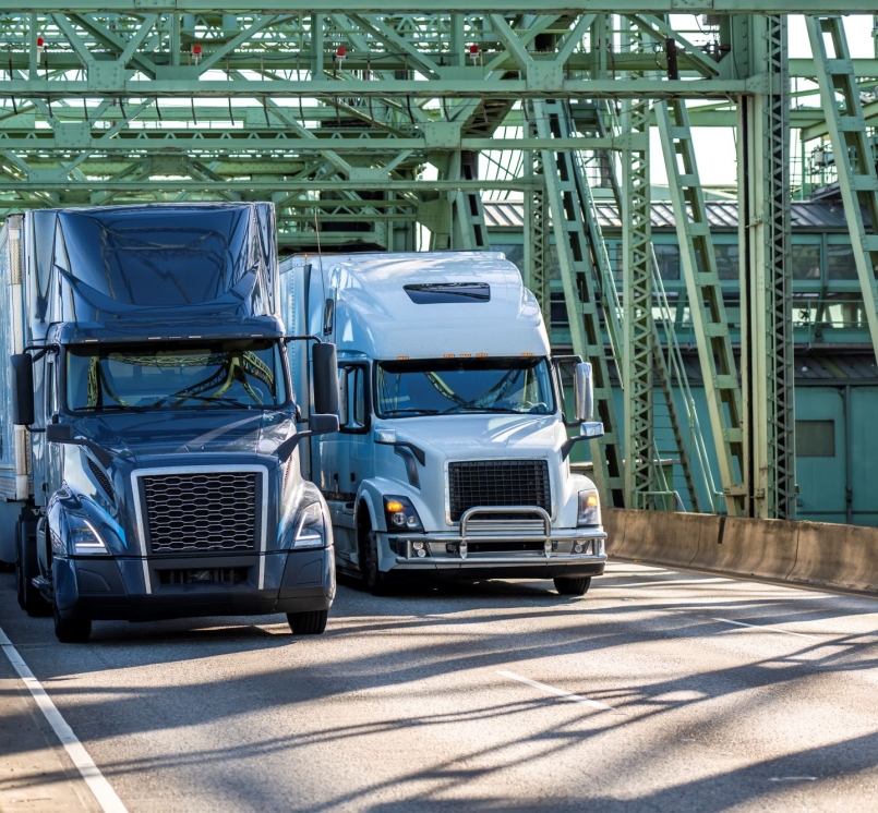 Industrial carriers blue and white big rig semi-truck tractors transporting cargo on dry van semi-trailers running on the truss metal arch I-5 Interstate Bridge between Washington and Oregon across  the Columbia River.