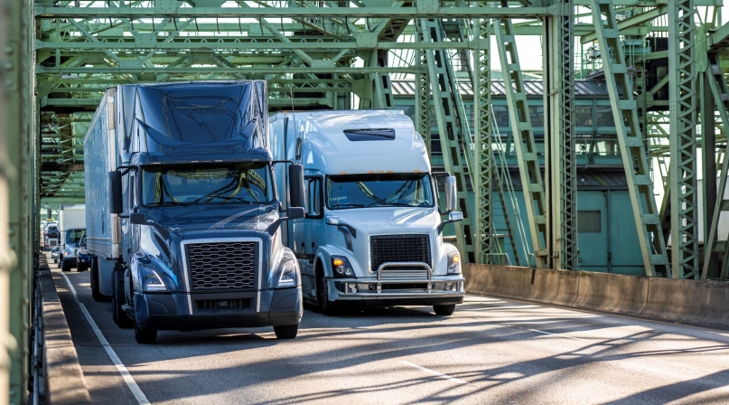 Industrial carriers blue and white big rig semi-truck tractors transporting cargo on dry van semi-trailers running on the truss metal arch I-5 Interstate Bridge between Washington and Oregon across  the Columbia River.