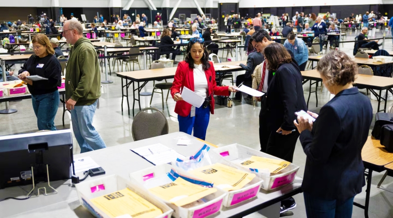 Paulina Gutiérrez, executive director of the Milwaukee Election Commission, middle, works on securing the tabulation machines after learning that the doors of the machines at the central counting facility at the Baird Center were not properly sealed on Election Day, Nov. 5, 2024. Joe Timmerman / Wisconsin Watch